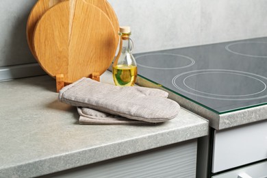 Photo of Oven glove, potholder, cutting boards and oil on grey countertop in kitchen