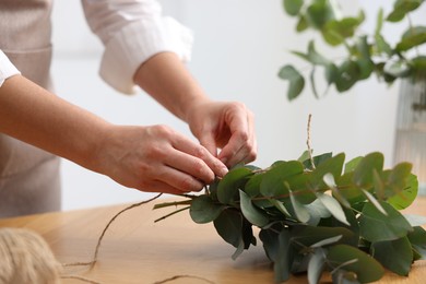 Photo of Florist making beautiful bouquet of eucalyptus branches at wooden table in flower shop, closeup