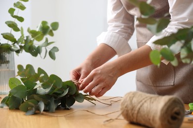 Photo of Florist making beautiful bouquet of eucalyptus branches at wooden table in flower shop, closeup