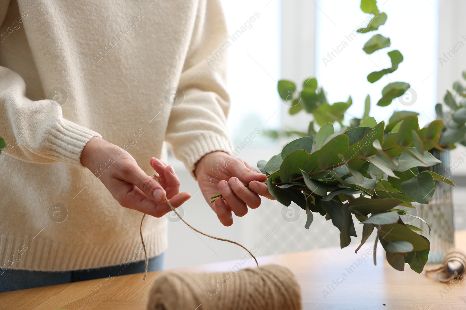 Florist with spool of thread making beautiful bouquet of eucalyptus branches at wooden table in flower shop, closeup Photo of Florist with spool of thread making beautiful bouquet of eucalyptus branches at wooden table in flower shop, closeup