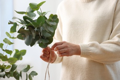 Photo of Florist making beautiful bouquet of eucalyptus branches in flower shop, closeup