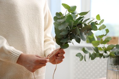 Photo of Florist making beautiful bouquet of eucalyptus branches in flower shop, closeup