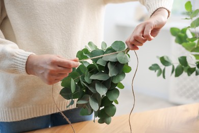Photo of Florist making beautiful bouquet of eucalyptus branches at wooden table in flower shop, closeup