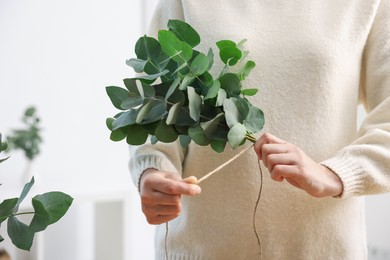 Photo of Florist making beautiful bouquet of eucalyptus branches in flower shop, closeup