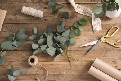 Photo of Florist. Eucalyptus branches, threads, ribbon, scissors and wrapping paper on wooden table, flat lay