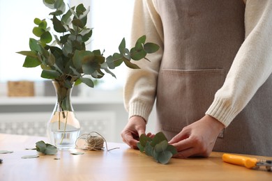 Photo of Florist making beautiful bouquet of eucalyptus branches at wooden table in flower shop, closeup