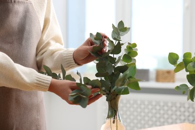 Photo of Florist making beautiful bouquet of eucalyptus branches in flower shop, closeup