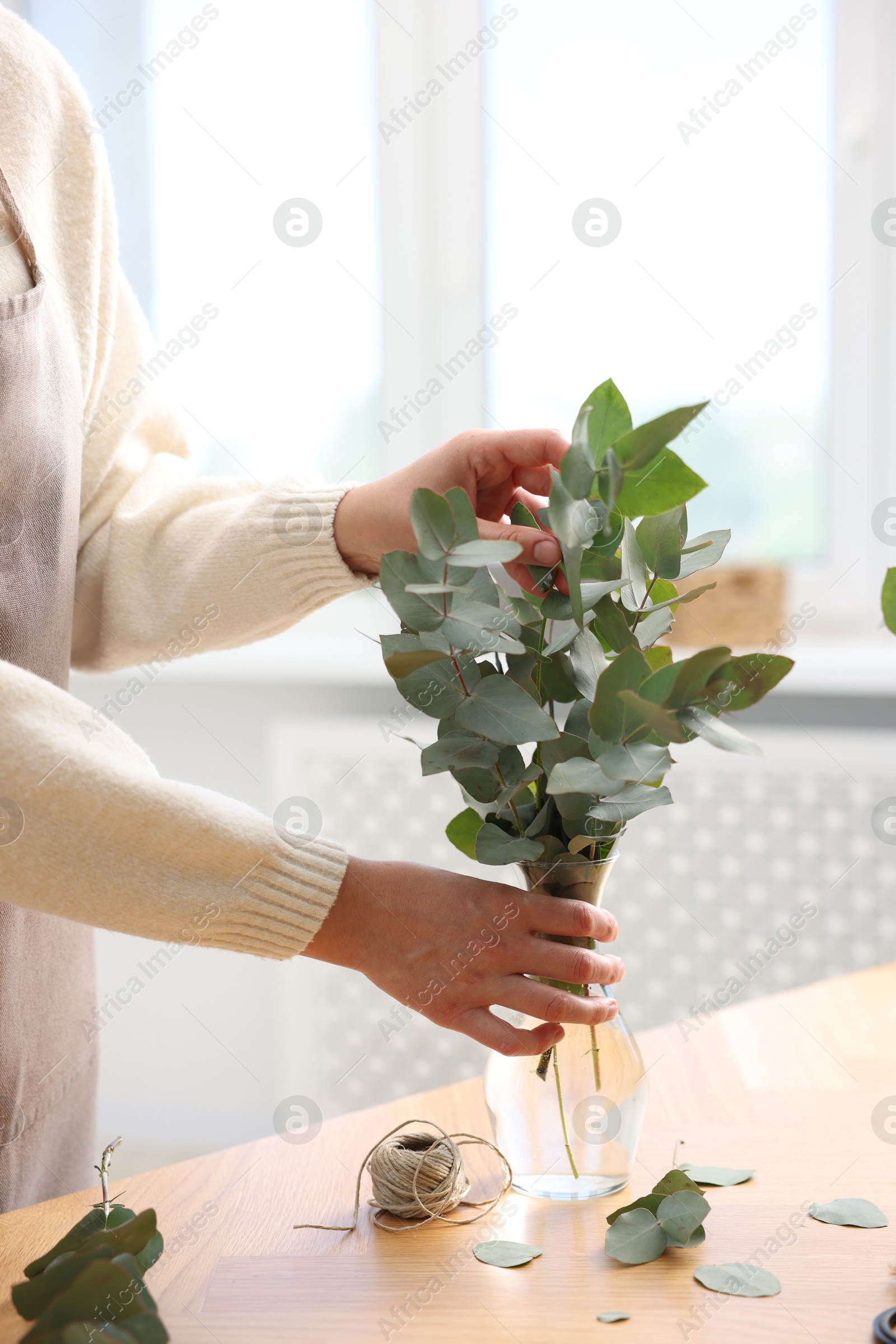 Photo of Florist making beautiful bouquet of eucalyptus branches at wooden table in flower shop, closeup