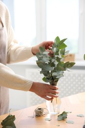 Photo of Florist making beautiful bouquet of eucalyptus branches at wooden table in flower shop, closeup