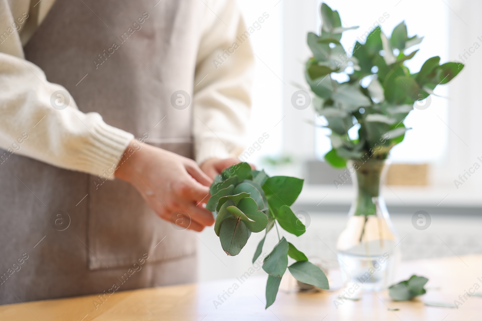 Photo of Florist making beautiful bouquet of eucalyptus branches at table in flower shop, closeup