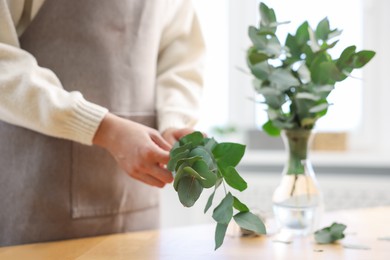 Photo of Florist making beautiful bouquet of eucalyptus branches at table in flower shop, closeup
