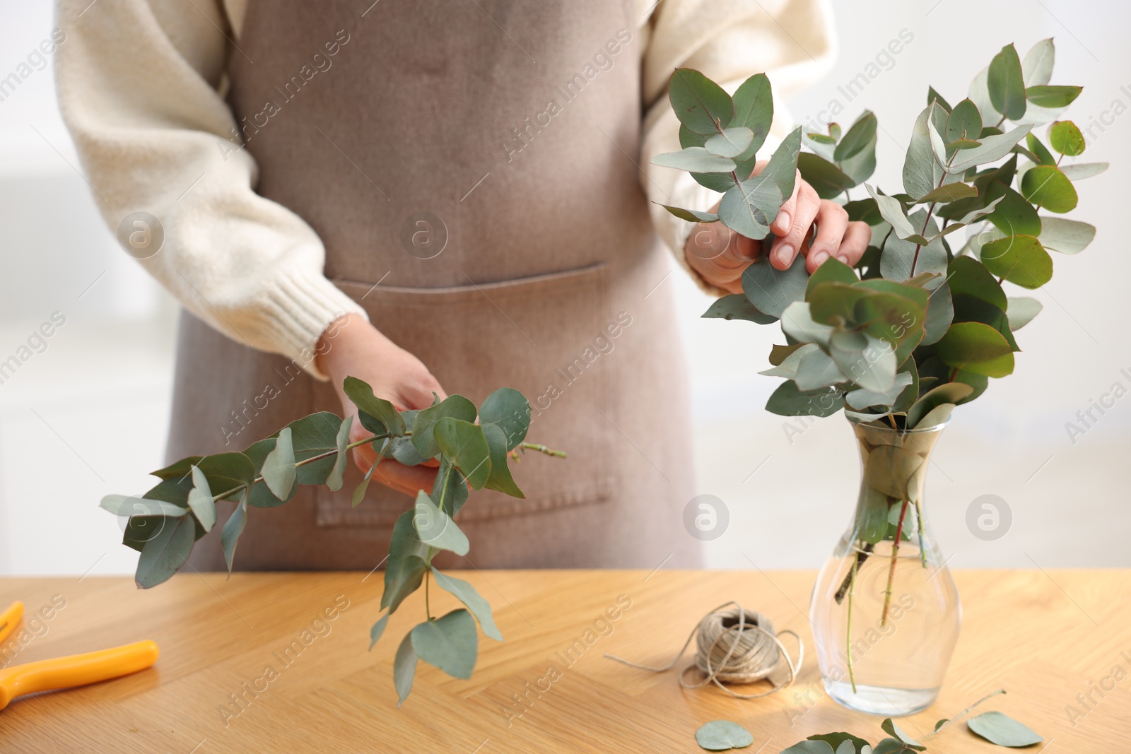 Photo of Florist making beautiful bouquet of eucalyptus branches at wooden table in flower shop, closeup