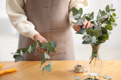 Photo of Florist making beautiful bouquet of eucalyptus branches at wooden table in flower shop, closeup