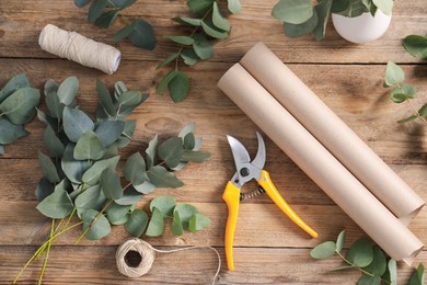Photo of Florist. Eucalyptus branches, threads, pruner and wrapping paper on wooden table, flat lay