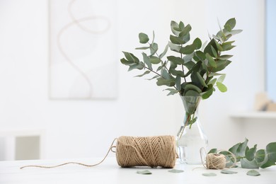 Photo of Florist. Eucalyptus branches in vase and threads on white table in flower shop, space for text