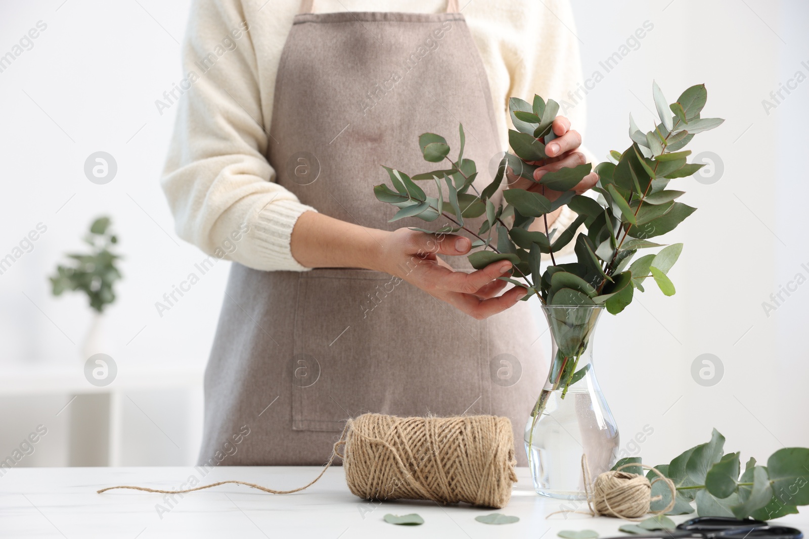 Florist making beautiful bouquet of eucalyptus branches at white marble table in flower shop, closeup Photo of Florist making beautiful bouquet of eucalyptus branches at white marble table in flower shop, closeup
