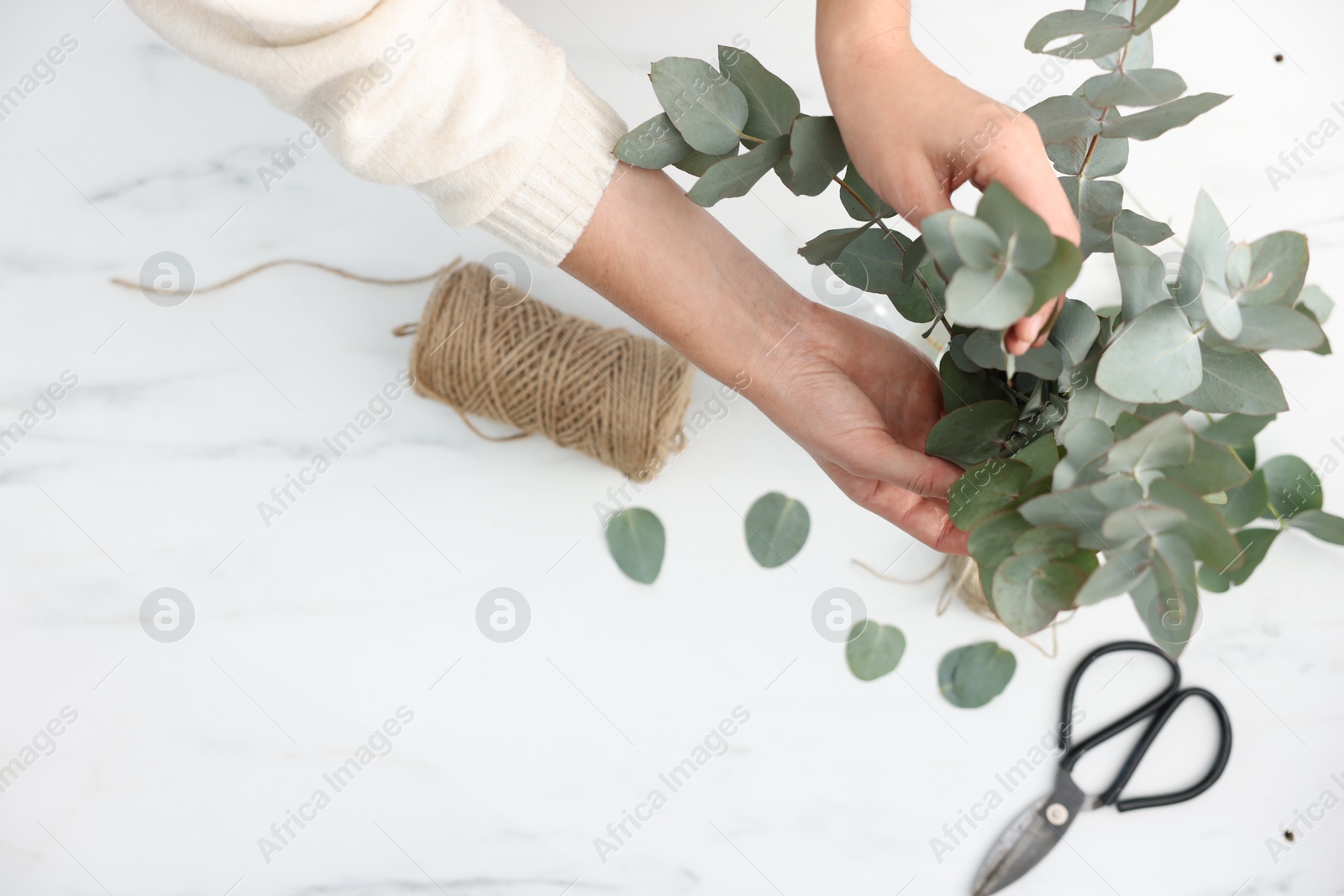 Photo of Florist making beautiful bouquet of eucalyptus branches at white marble table, top view. Space for text