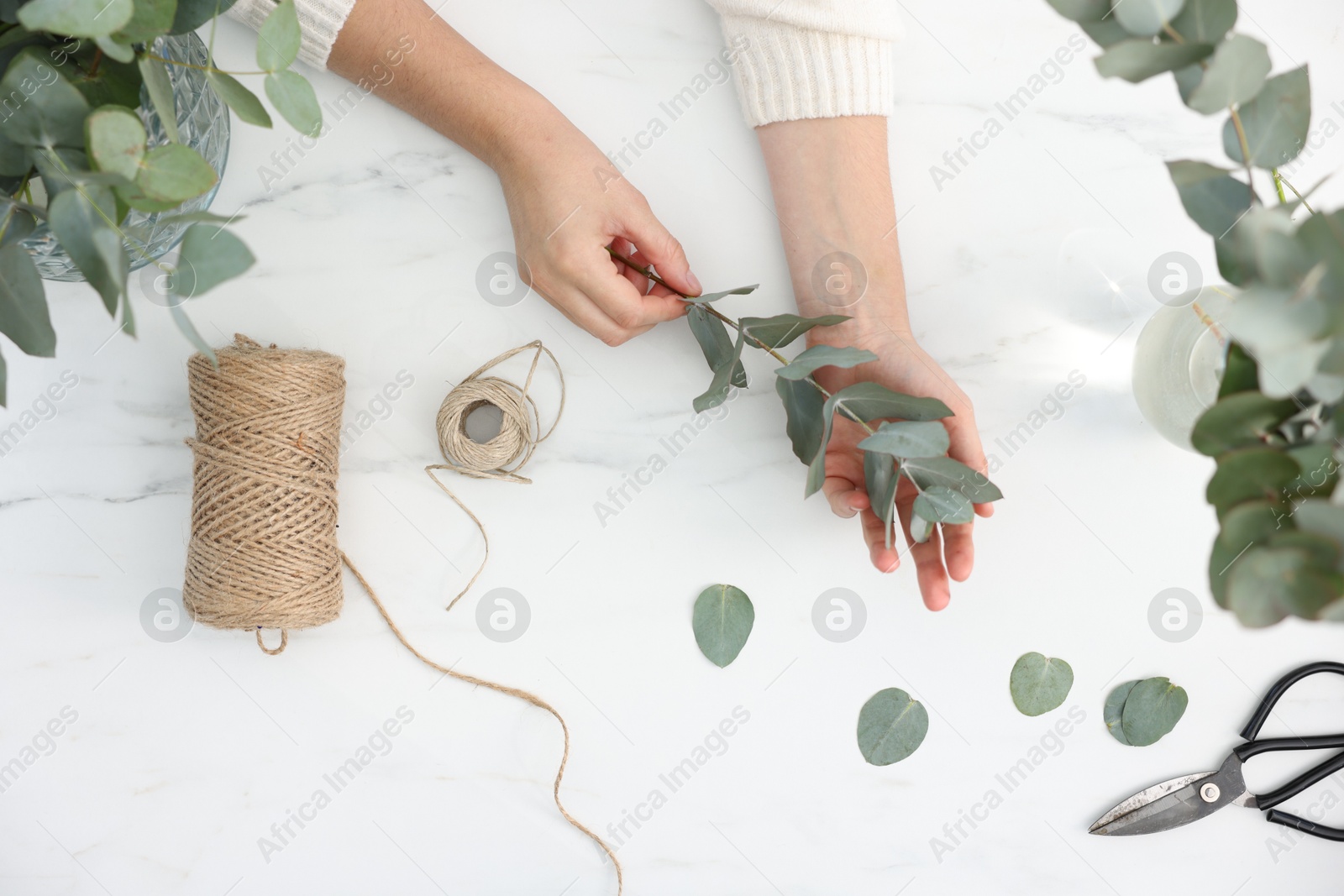 Photo of Florist making beautiful bouquet of eucalyptus branches at white marble table, top view