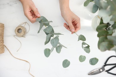 Photo of Florist making beautiful bouquet of eucalyptus branches at white marble table, top view