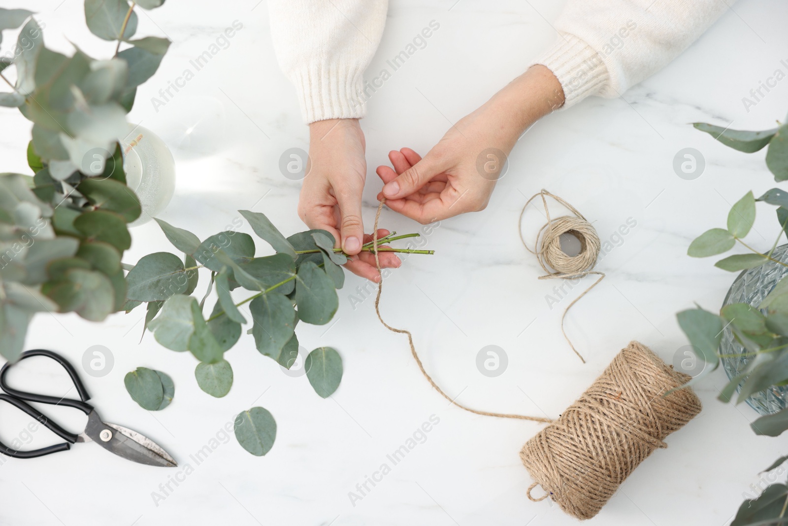 Florist making beautiful bouquet of eucalyptus branches at white marble table, top view Photo of Florist making beautiful bouquet of eucalyptus branches at white marble table, top view
