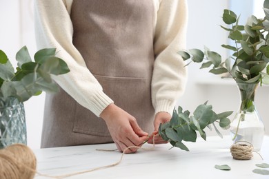 Photo of Florist making beautiful bouquet of eucalyptus branches at white marble table in flower shop, closeup