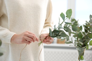 Photo of Florist making beautiful bouquet of eucalyptus branches in flower shop, closeup