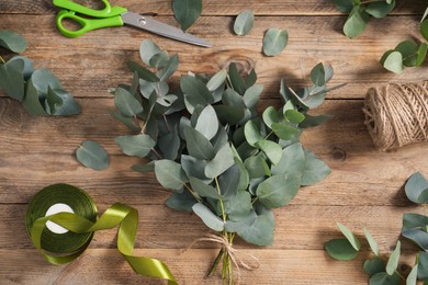 Photo of Florist. Eucalyptus branches, thread, ribbon and scissors on wooden table, flat lay