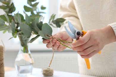Photo of Florist making beautiful bouquet of eucalyptus branches at table in flower shop, closeup