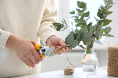 Photo of Florist making beautiful bouquet of eucalyptus branches at table in flower shop, closeup
