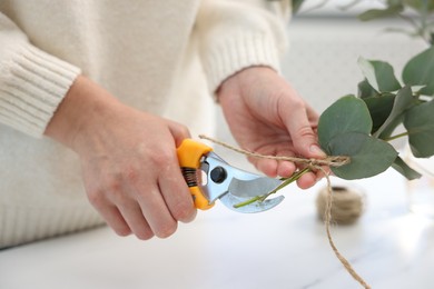 Photo of Florist making beautiful bouquet of eucalyptus branches at table in flower shop, closeup