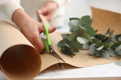Photo of Florist making beautiful bouquet of eucalyptus branches at white table in flower shop, closeup