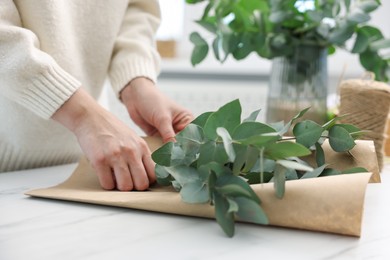 Photo of Florist making beautiful bouquet of eucalyptus branches at white marble table in flower shop, closeup
