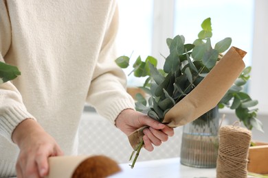 Photo of Florist making beautiful bouquet of eucalyptus branches at white table in flower shop, closeup