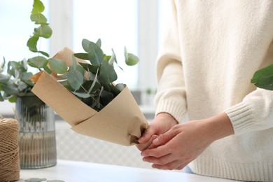Photo of Florist making beautiful bouquet of eucalyptus branches at white table in flower shop, closeup