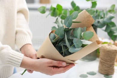 Photo of Florist making beautiful bouquet of eucalyptus branches at table in flower shop, closeup