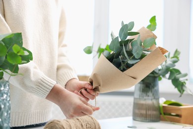 Photo of Florist making beautiful bouquet of eucalyptus branches at table in flower shop, closeup