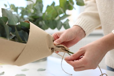 Photo of Florist making beautiful bouquet of eucalyptus branches at table in flower shop, closeup