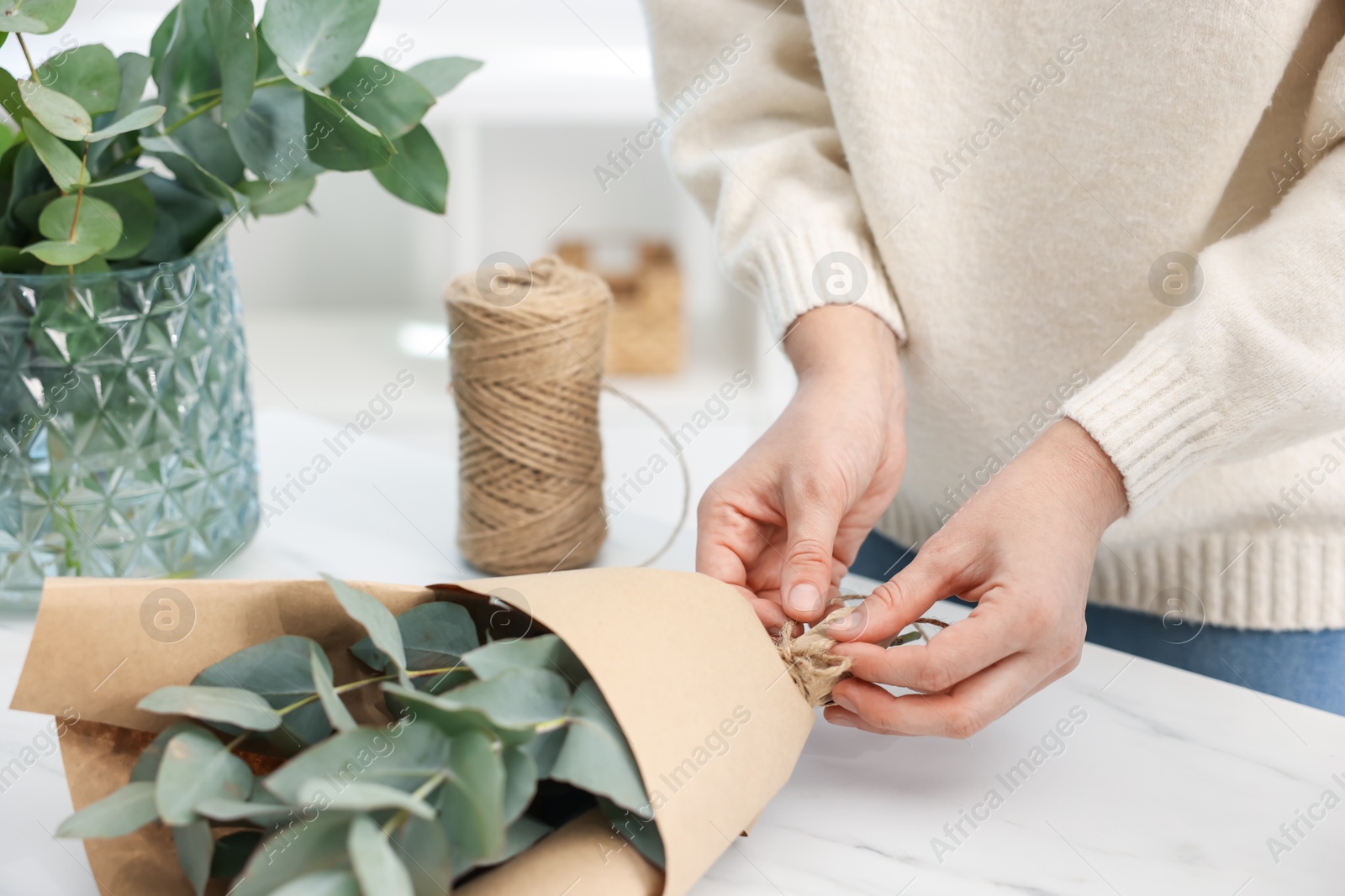 Florist making beautiful bouquet of eucalyptus branches at white marble table in flower shop, closeup Photo of Florist making beautiful bouquet of eucalyptus branches at white marble table in flower shop, closeup