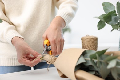 Photo of Florist making beautiful bouquet of eucalyptus branches at white marble table in flower shop, closeup