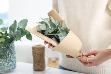 Photo of Florist making beautiful bouquet of eucalyptus branches at table in flower shop, closeup