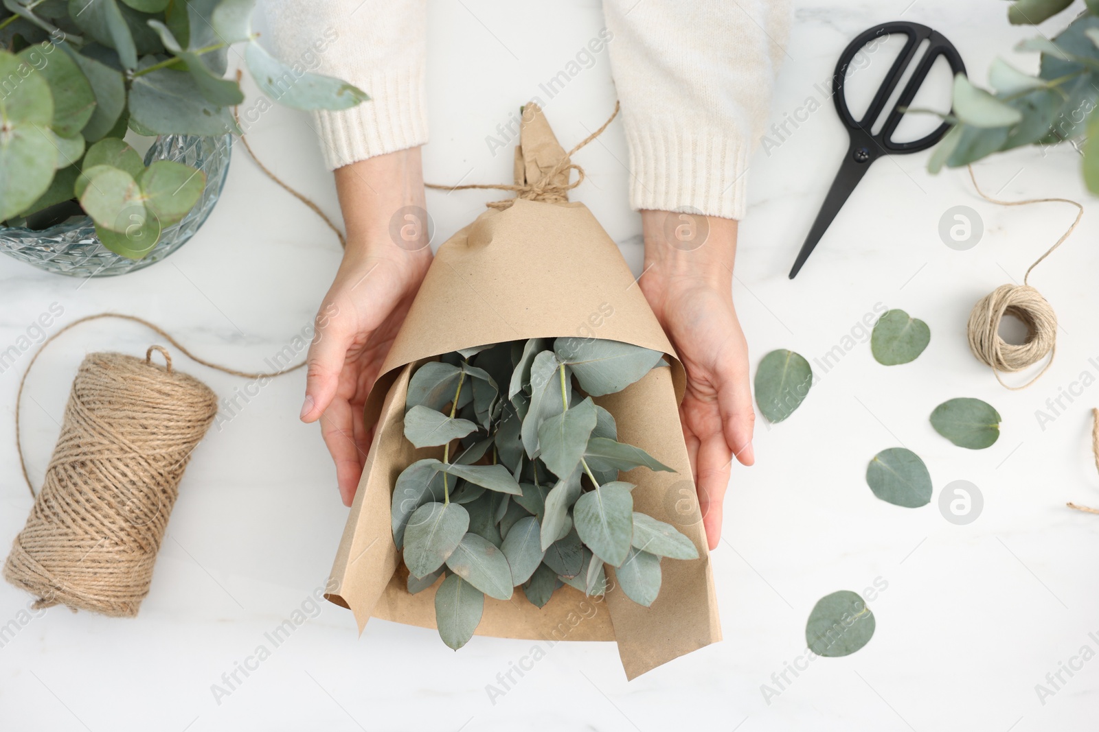 Florist making beautiful bouquet of eucalyptus branches at white marble table, top view Photo of Florist making beautiful bouquet of eucalyptus branches at white marble table, top view