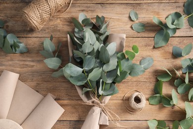 Photo of Florist. Eucalyptus branches, threads and wrapping paper on wooden table, flat lay