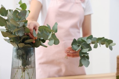 Photo of Florist making beautiful bouquet of eucalyptus branches at table in flower shop, closeup