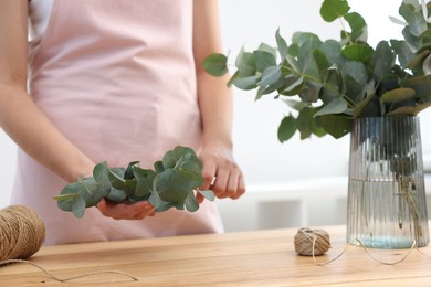 Photo of Florist making beautiful bouquet of eucalyptus branches at wooden table in flower shop, closeup