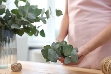 Photo of Florist making beautiful bouquet of eucalyptus branches at wooden table in flower shop, closeup