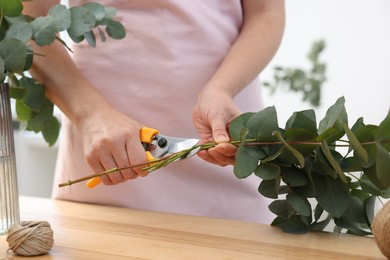 Photo of Florist making beautiful bouquet of eucalyptus branches at wooden table in flower shop, closeup