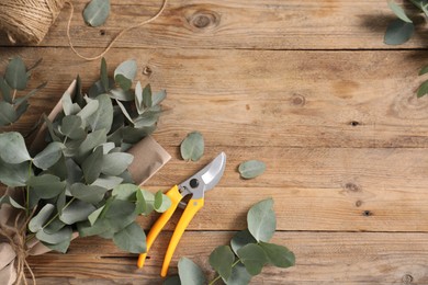 Photo of Florist. Eucalyptus branches, threads, pruner and wrapping paper on wooden table, flat lay. Space for text