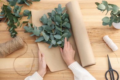 Photo of Florist making beautiful bouquet of eucalyptus branches at wooden table, top view