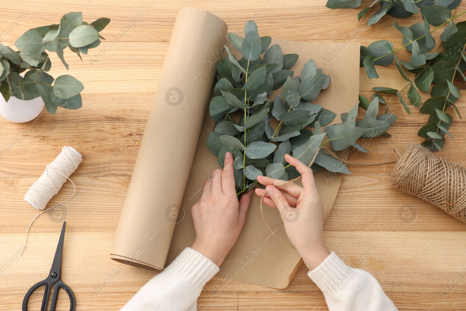 Florist making beautiful bouquet of eucalyptus branches at wooden table, top view Photo of Florist making beautiful bouquet of eucalyptus branches at wooden table, top view
