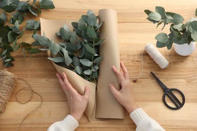 Photo of Florist making beautiful bouquet of eucalyptus branches at wooden table, top view